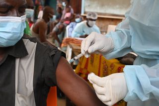 close up of a gloved nurse injecting an ebola vaccine into a sitting patient's arm