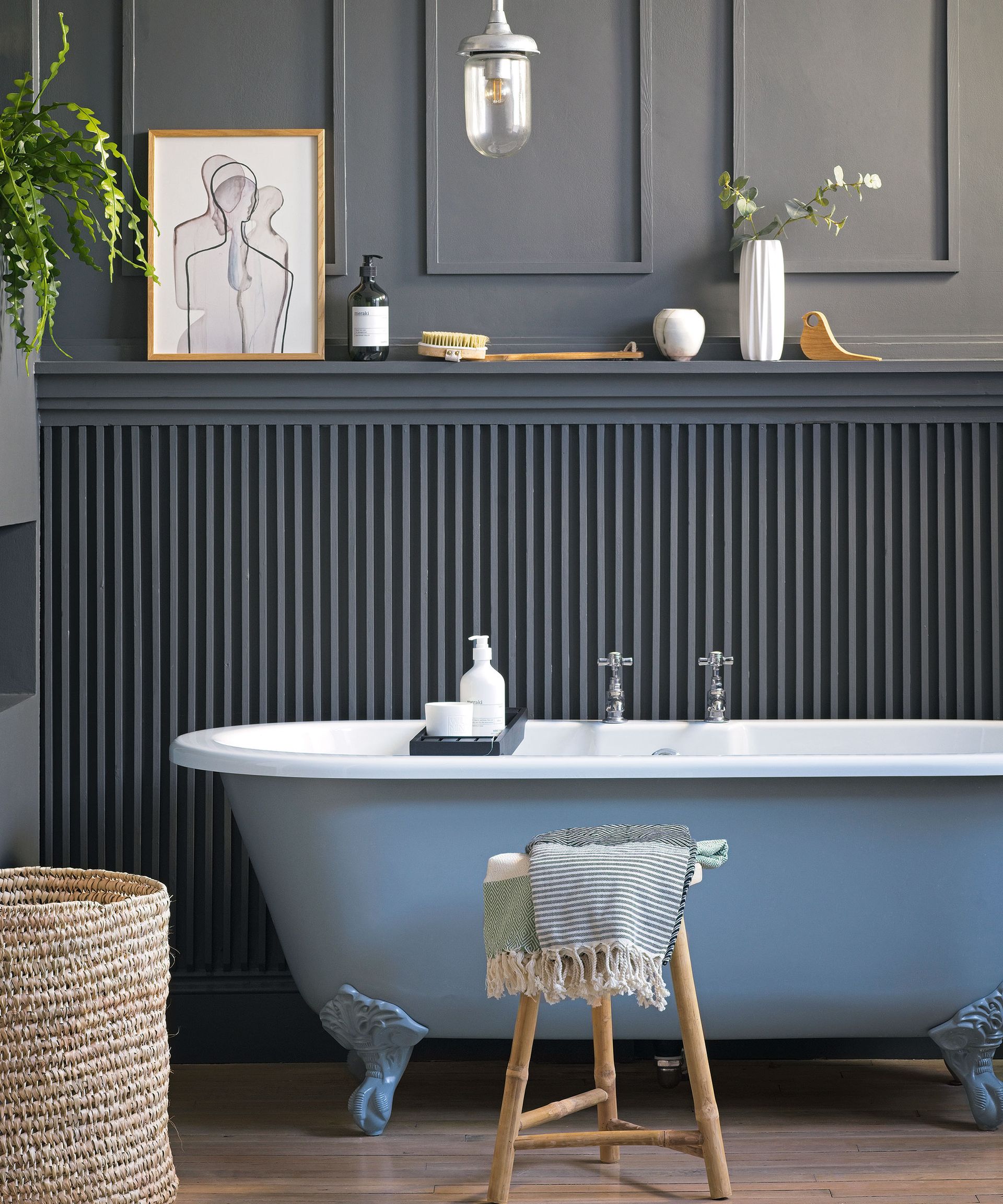 Freestanding bath in front of wooden paneled painted wall with decorative plants and towels