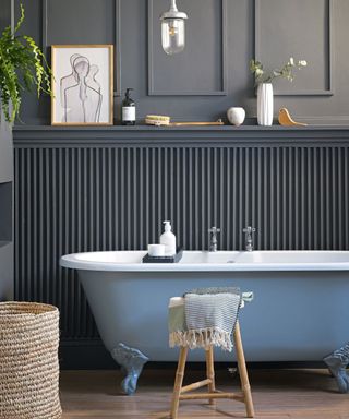 Freestanding bath in front of wooden panelled painted wall with decorative plants and towels