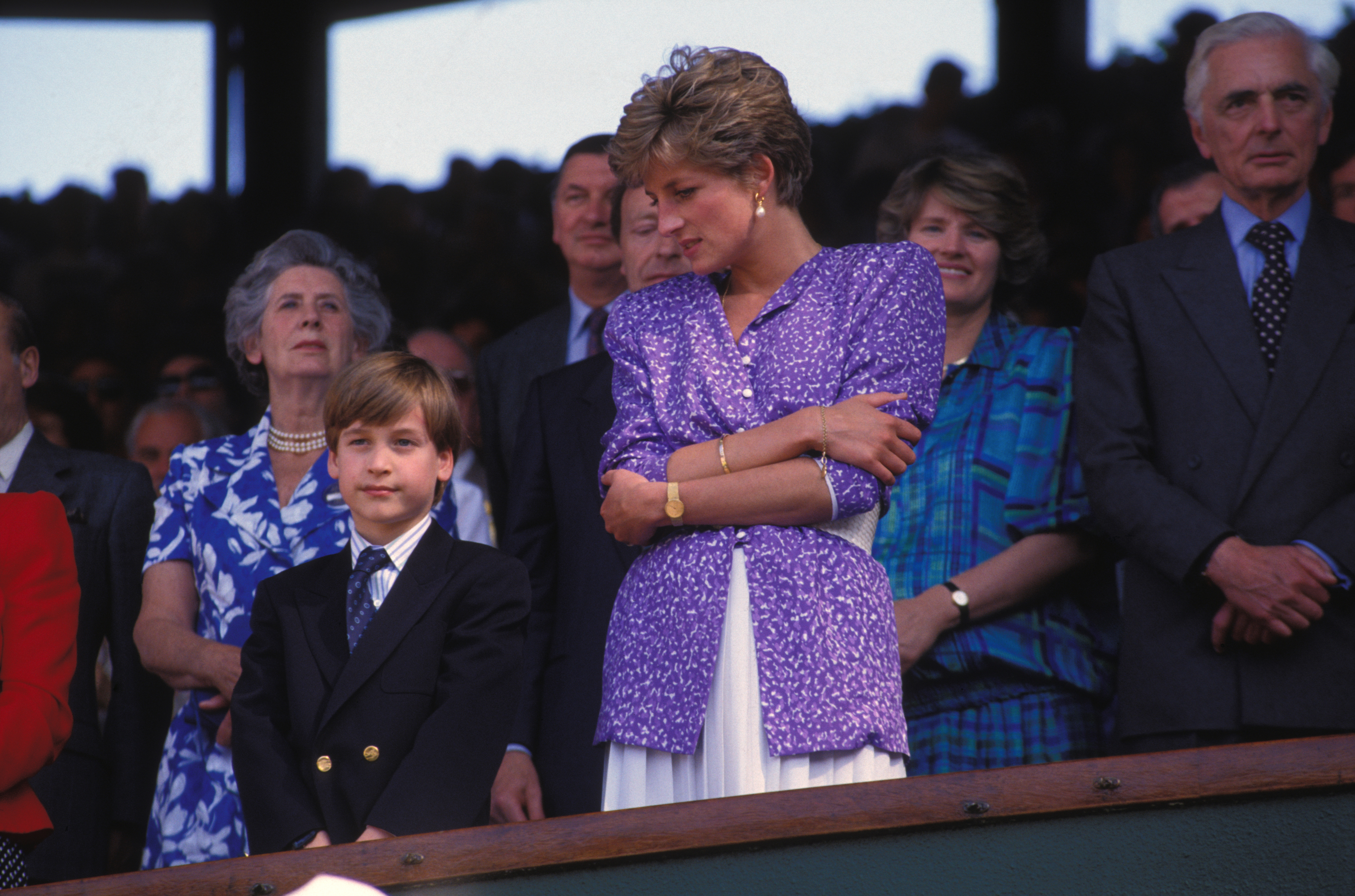 Prince William in a navy suit and Princess Diana, in a purple blazer, standing next to each other at Wimbledon 1991