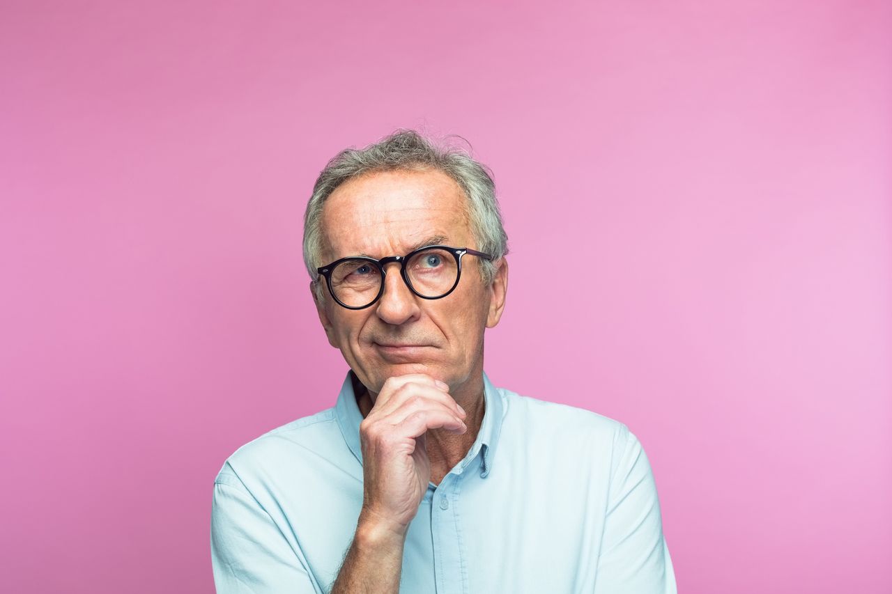 Confused retired man with hand on chin looking away 