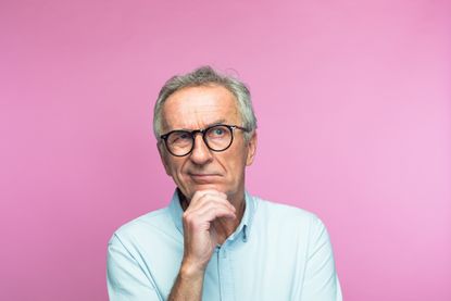 Confused retired man with hand on chin looking away 