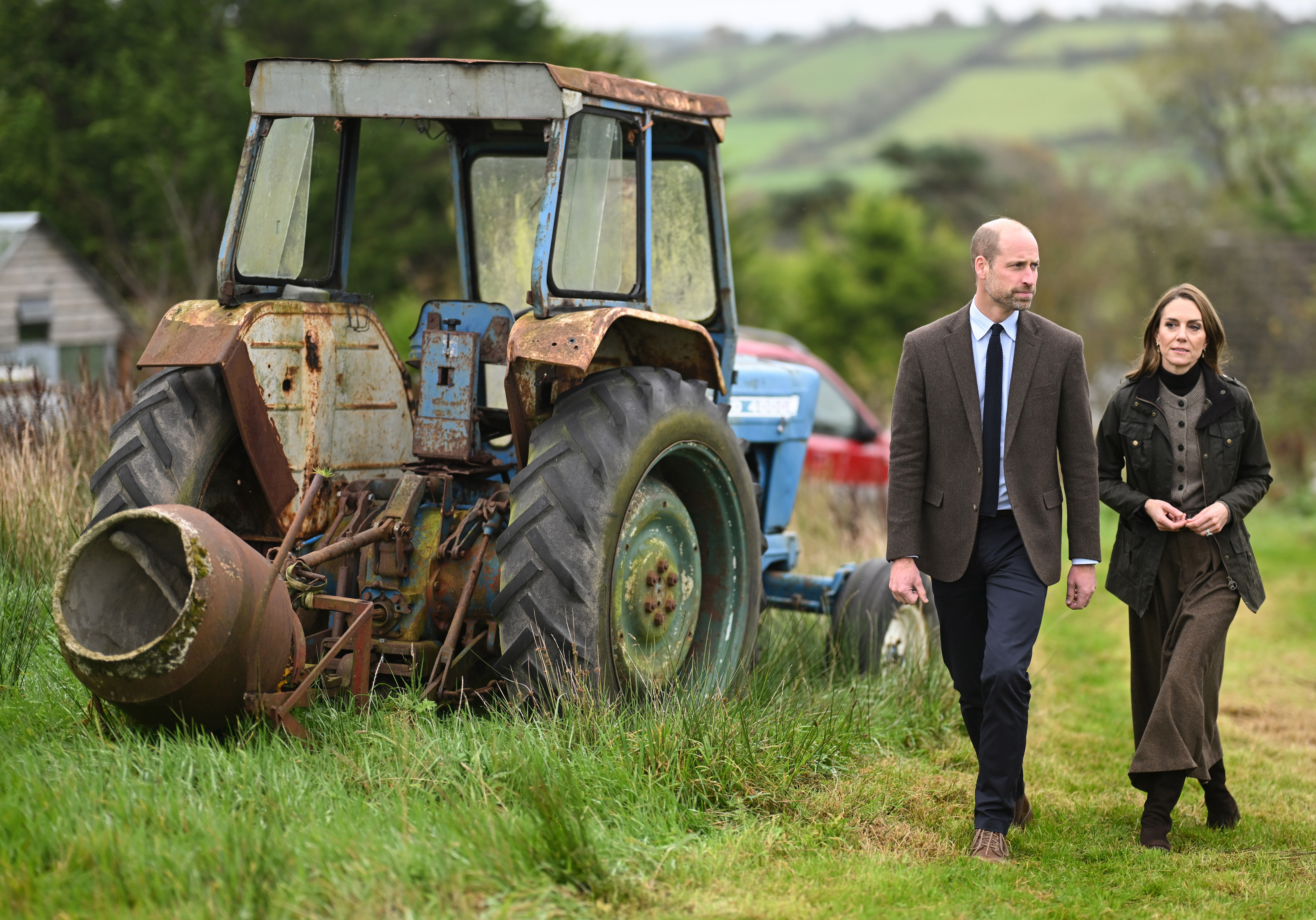 Prince William and Princess Kate walking by a tractor, wearing brown outfits