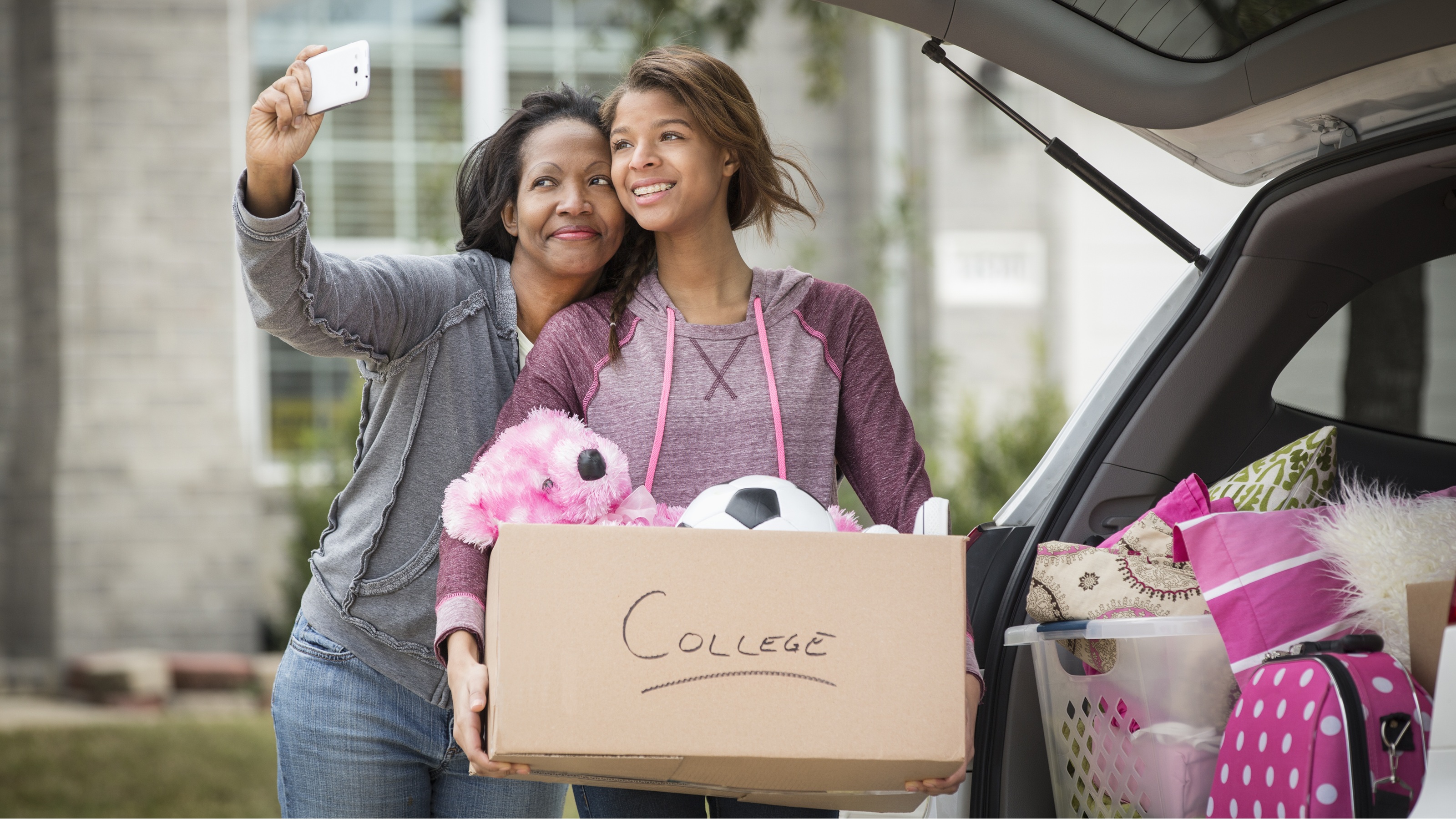 A mom takes a selfie with her daughter, who&#039;s holding a box that says college.