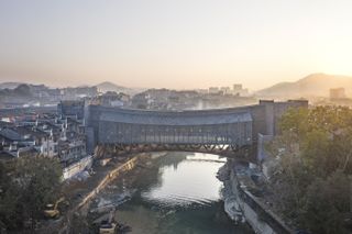 Jishou Art Museum is set over a river. It resembles a covered bridge. We see the rest of the town on both sides, and the photo is taken at sunset.