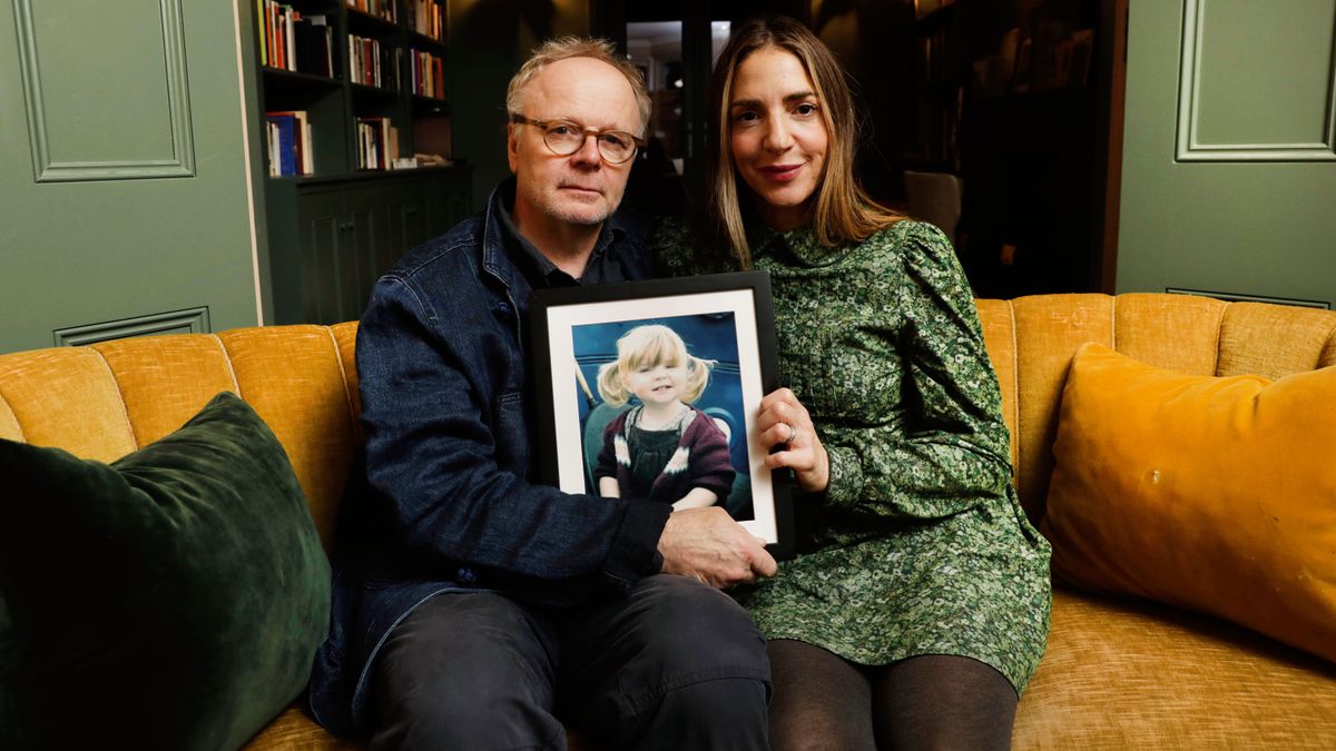 Jason and Clara sitting together holding a photo of their daughter, Maudie