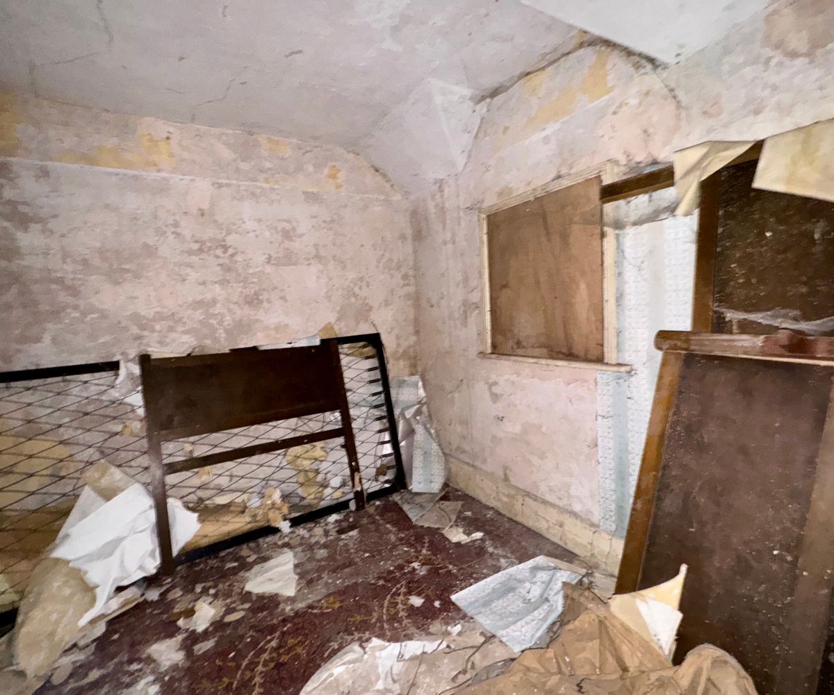 A bedroom that has cracked walls and boarded up windows