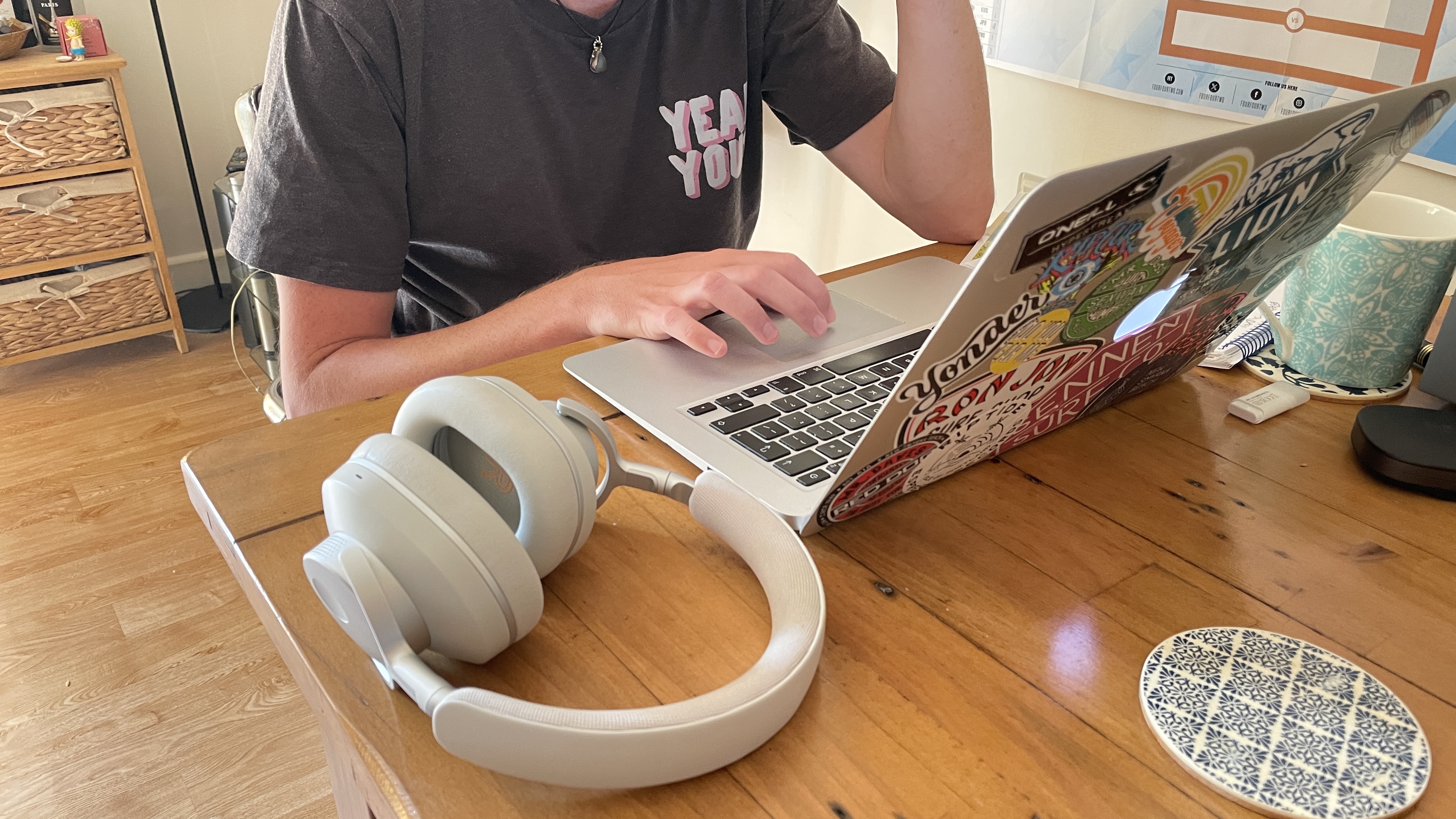 An image of Cambridge Audio headphones on a desk, with a very handsome man on a laptop in the background He is wearing an excellent 'Yeah You' T-shirt his fiance bought him