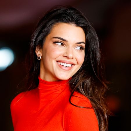 Kendall Jenner has long dark brown hair and wears a bright red turtle neck dress