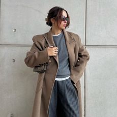 a woman wearing a brown coat, gray sweater, and gray striped pants 