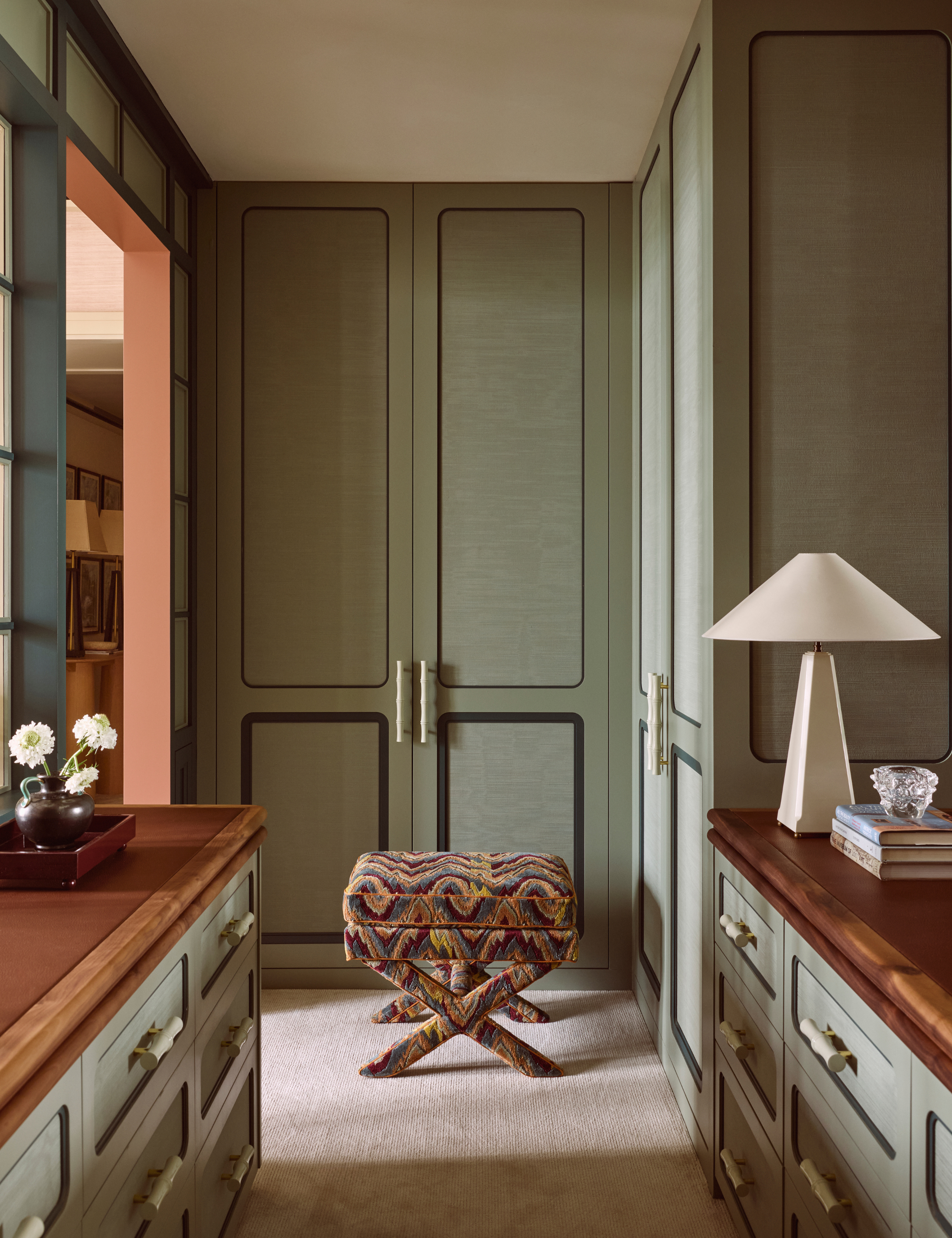 Tranquil dressing room area featuring moss green built-in closetry, anchored by a technicolor patterned ottoman and a whisper-light beige carpet