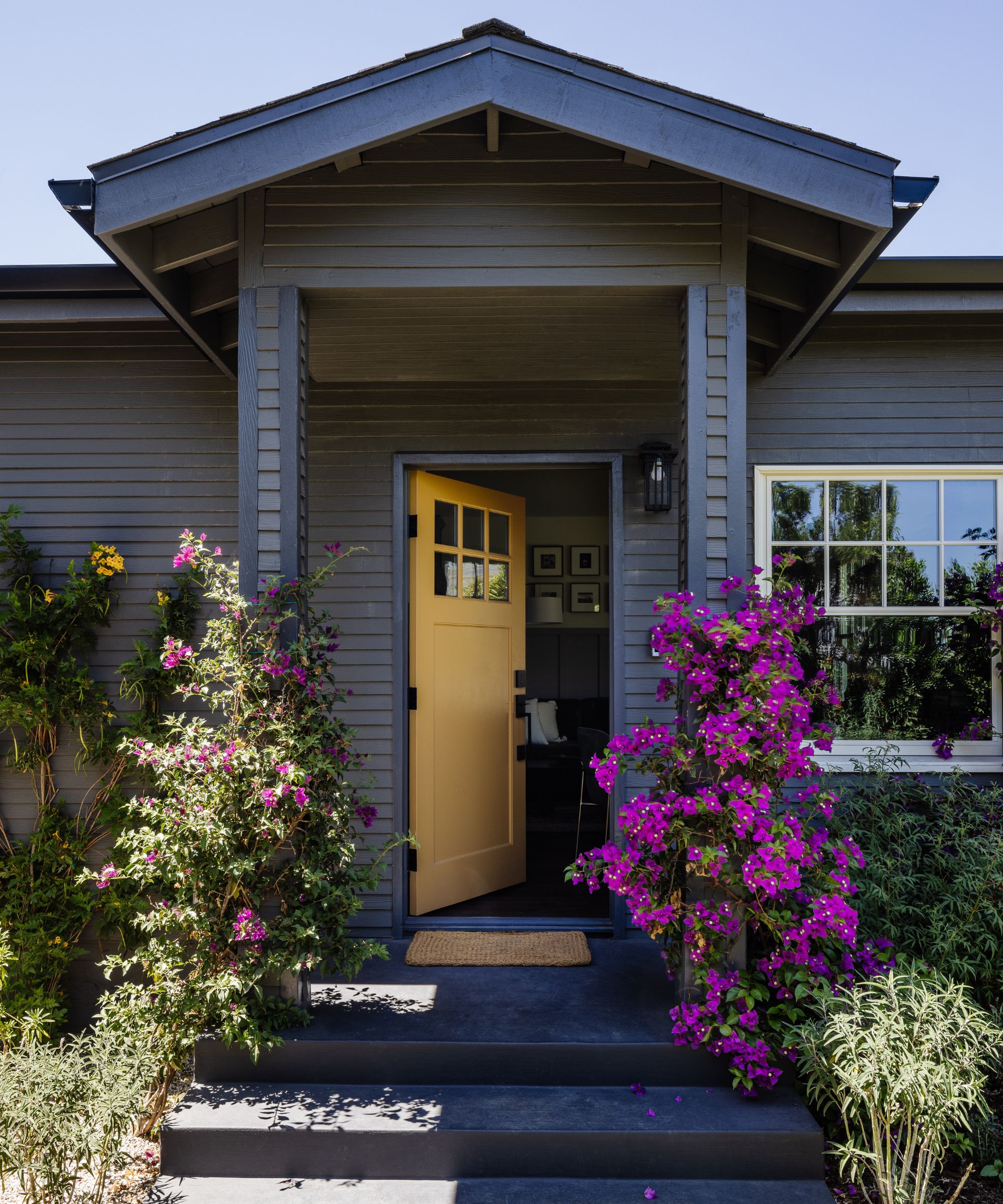 House with grey wood panelling, yellow front door and purple flowers