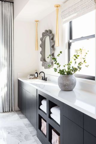 A white bathroom with large black vanity and brass lights either side of the mirror