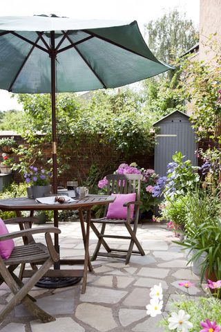 patio space with dining table, chairs and a parasol with pink cushions and flowers