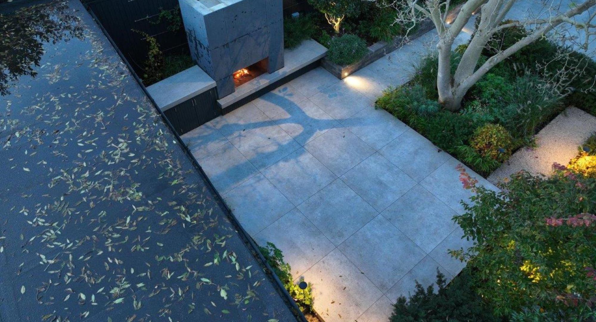 Aerial shot of an urban grey and green patio garden lit up at night with LED lights casting shadows on the ground.