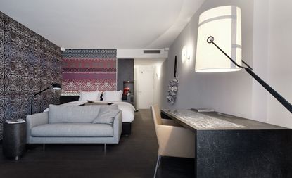 Room with bed, couch, desk with single chair and lamp, patterned wallpaper