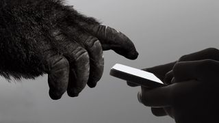 A person holding a phone, and a gorilla's hand is reaching out, pointing to the phone