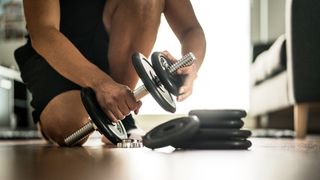Man adds weight plate to adjustable dumbbell at home