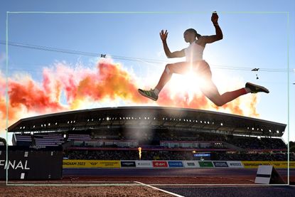 An athlete at the Commonwealth Games mid long jump and back lit by the sun