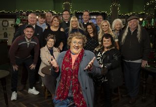 The cast of Mrs Brown's Boys in character, with Mrs Brown at the front and everyone smiling behind her.