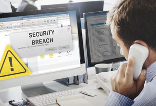 An employee on the phone while his computer screen shows "cyber attack" warning