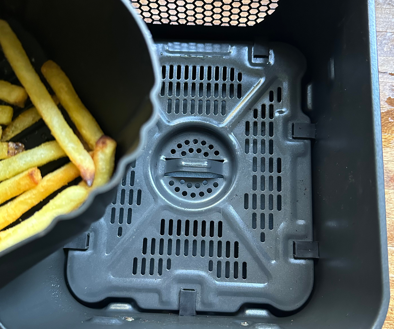 A clean, empty air fryer basket with the corner of a silicone air fryer basket liner filled with fries visible to the side.