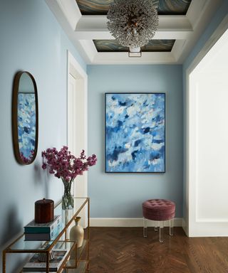 Entryway with distinctive blue piece of art and florals positioned in front of mirror