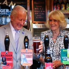 Queen Camilla and King Charles laughing as they pull pints at a pub