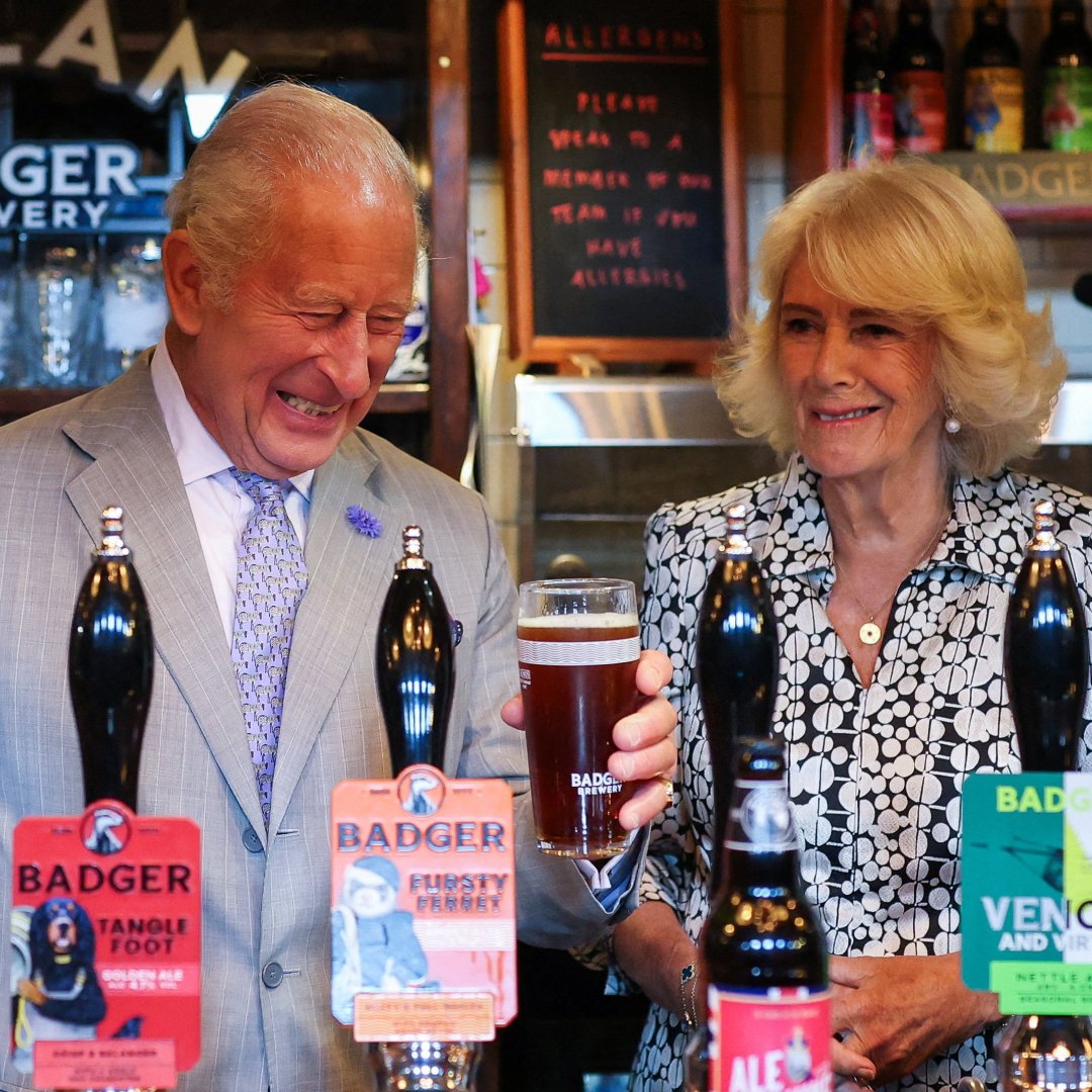 Queen Camilla and King Charles laughing as they pull pints at a pub