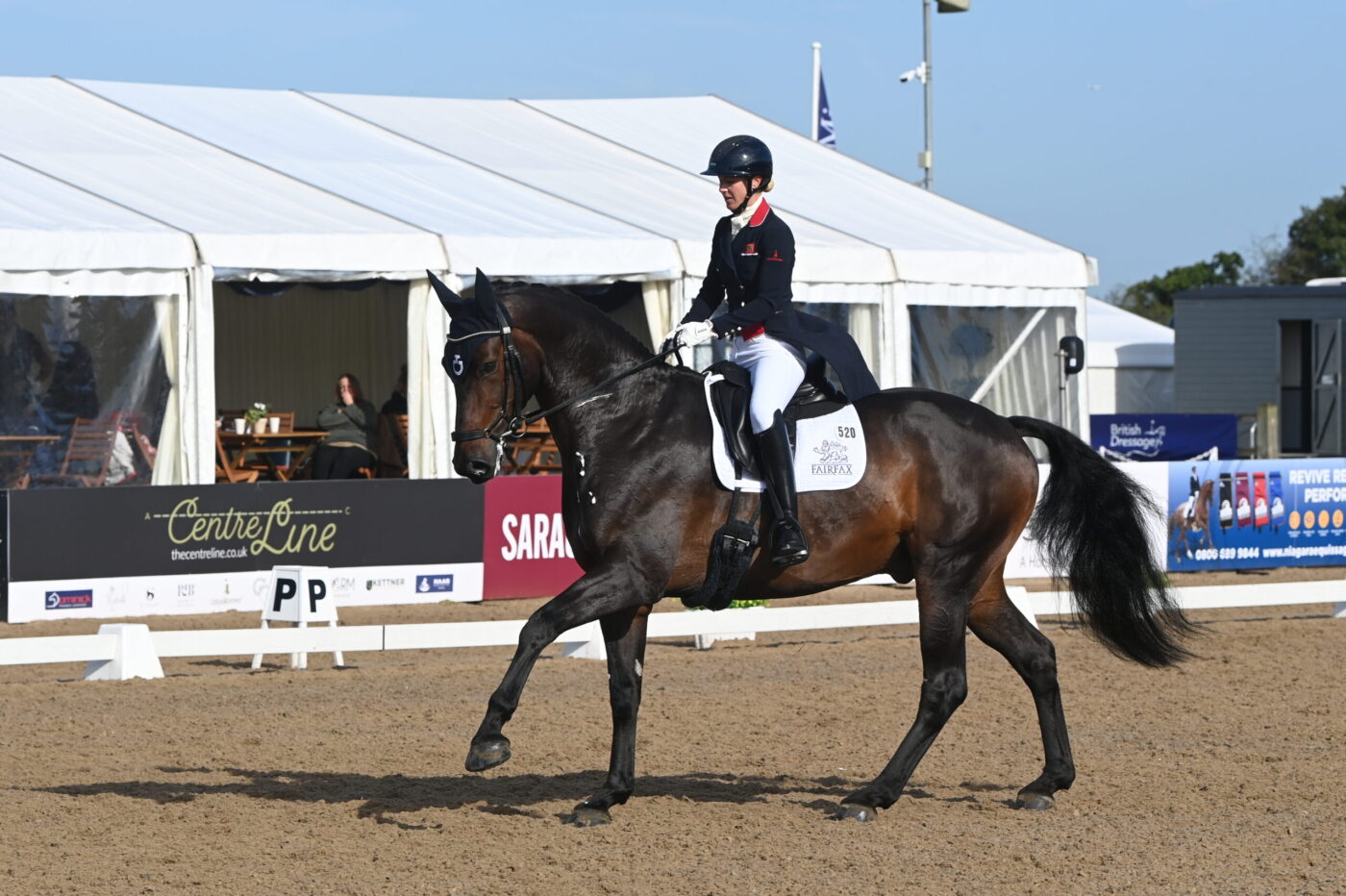 Laura Tomlinson cantering in an outdoor arena on a bay horse,