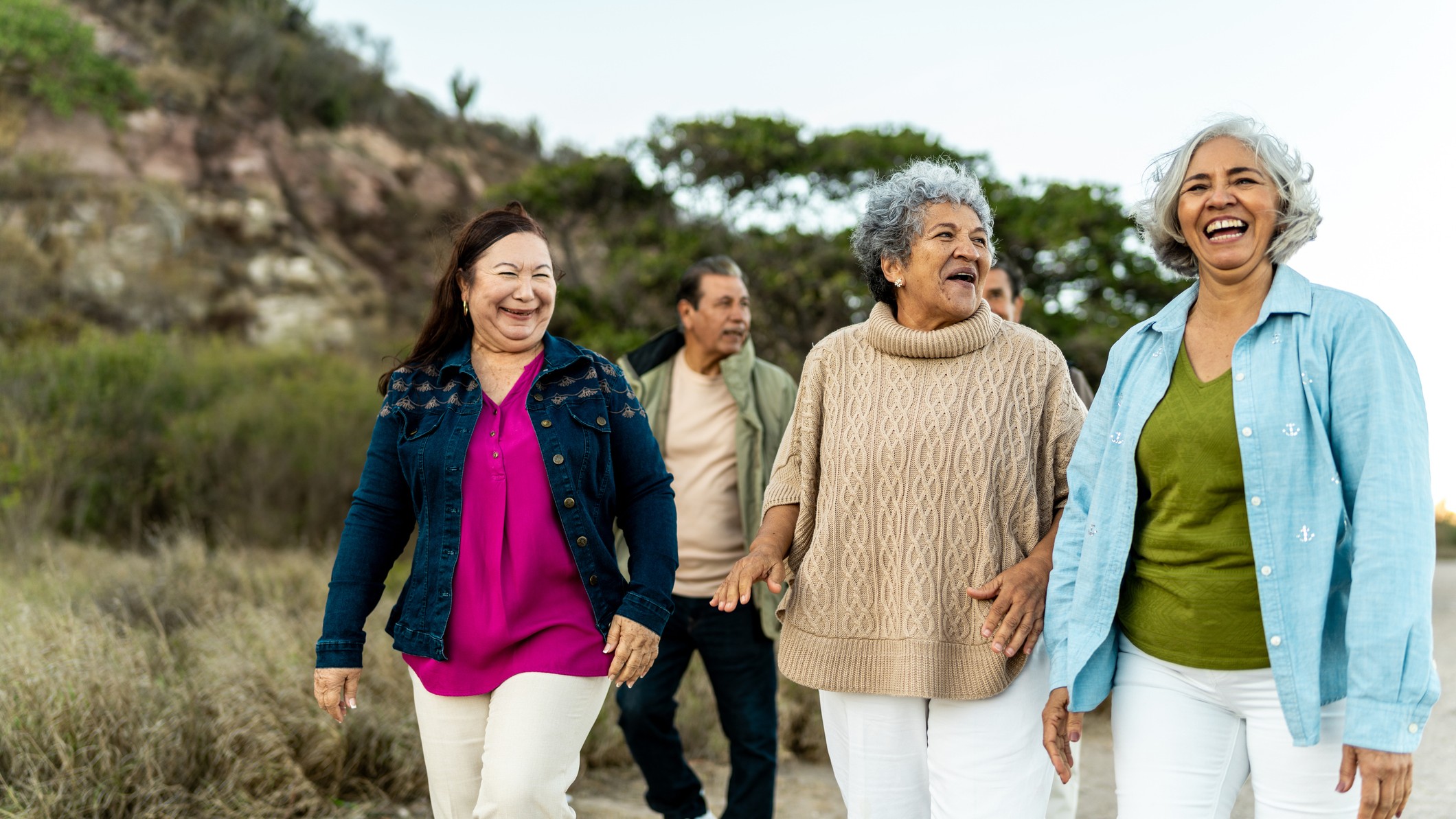 A group of three older women walk together, chatting and laughing. Behind them two older men can be seen too.