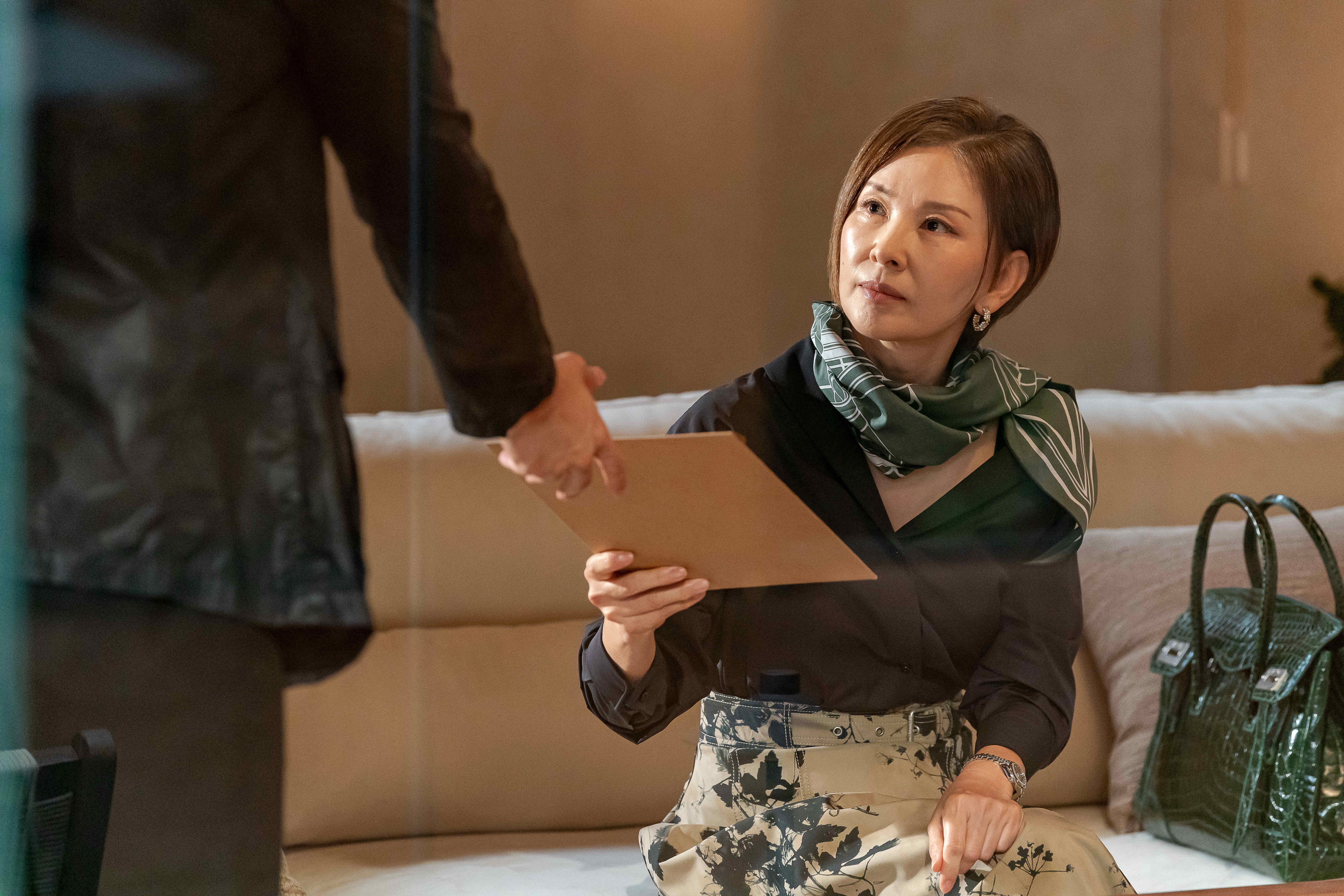 Lee Mi-sook takes a folder from a man&#039;s hand in &#039;Tempest.&#039;