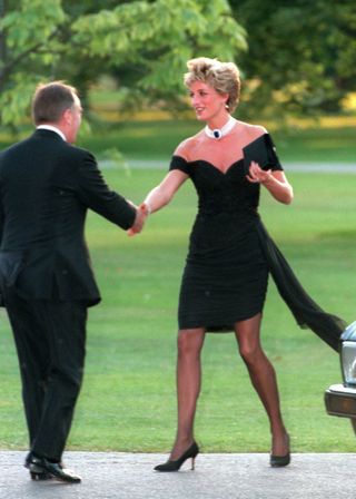 Princess Diana wearing her short black revenge dress and shaking hands with a man with grass behind her