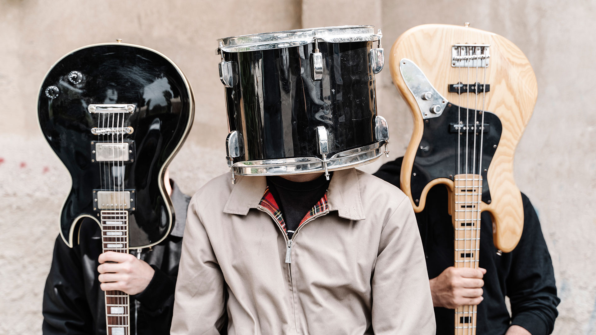 Three musicians, with faces obscured by their instruments &amp;ndash;&amp;nbsp;L-R guitarist, drummer and bassist