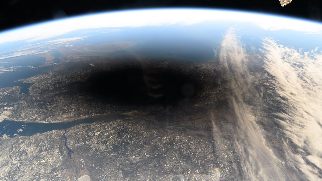 Η σκιά του φεγγαριού εμφανίζεται ως μια μαύρη κουκκίδα πάνω από τα χιονισμένα μέρη του Καναδά και του Μέιν του διαστημικού σταθμού, με ορισμένα από τα όργανα του σταθμού ορατά
