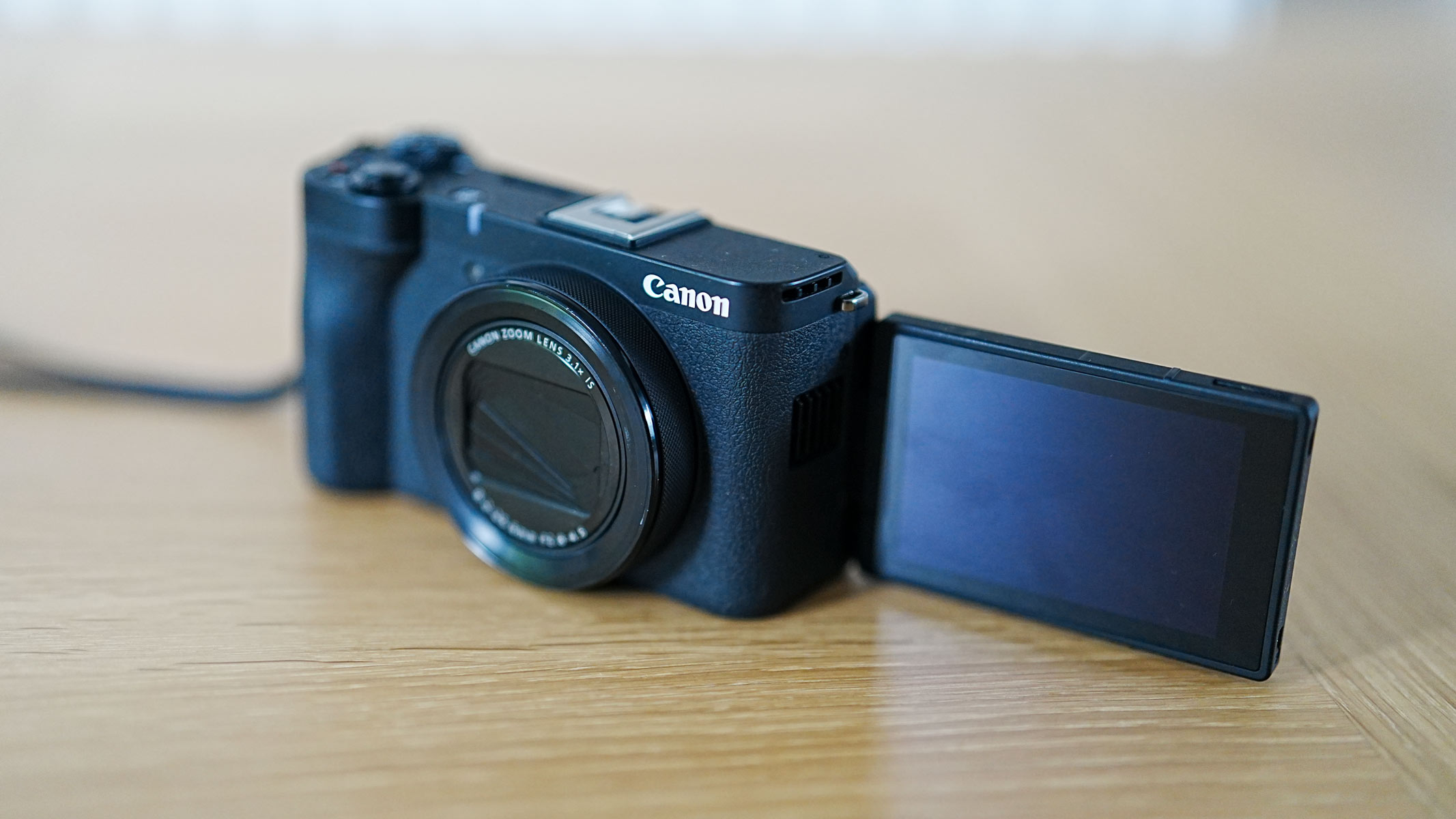 The Canon Powershot V1 on a wooden table with shutter closed and screen flipped out to the side.