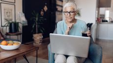A smiling older woman sits with her laptop open on her lap.