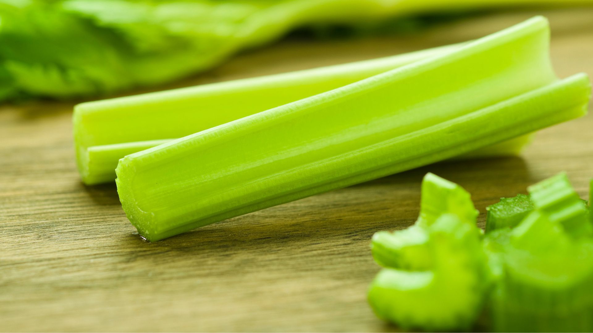 Whole and chopped celery sitting on wooden counter