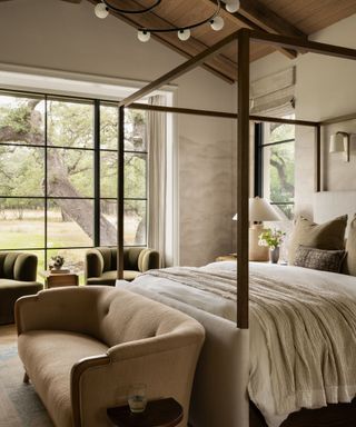 Neutral bedroom with wooden canopy bed, brown sofa, green armchairs and large windows