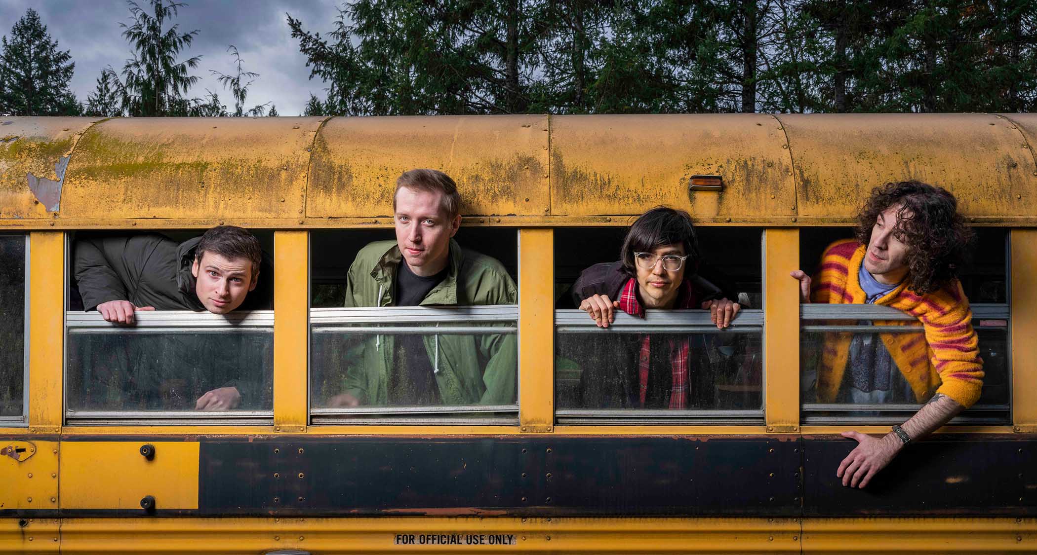 The members of Seattle-based indie-rock band Car Seat Headrest hang-out of the side of a yellow school bus.