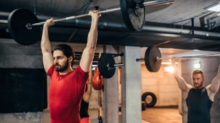 Group perform overhead press exercise with barbell