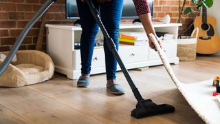 woman picking up rug to vacuum underneath