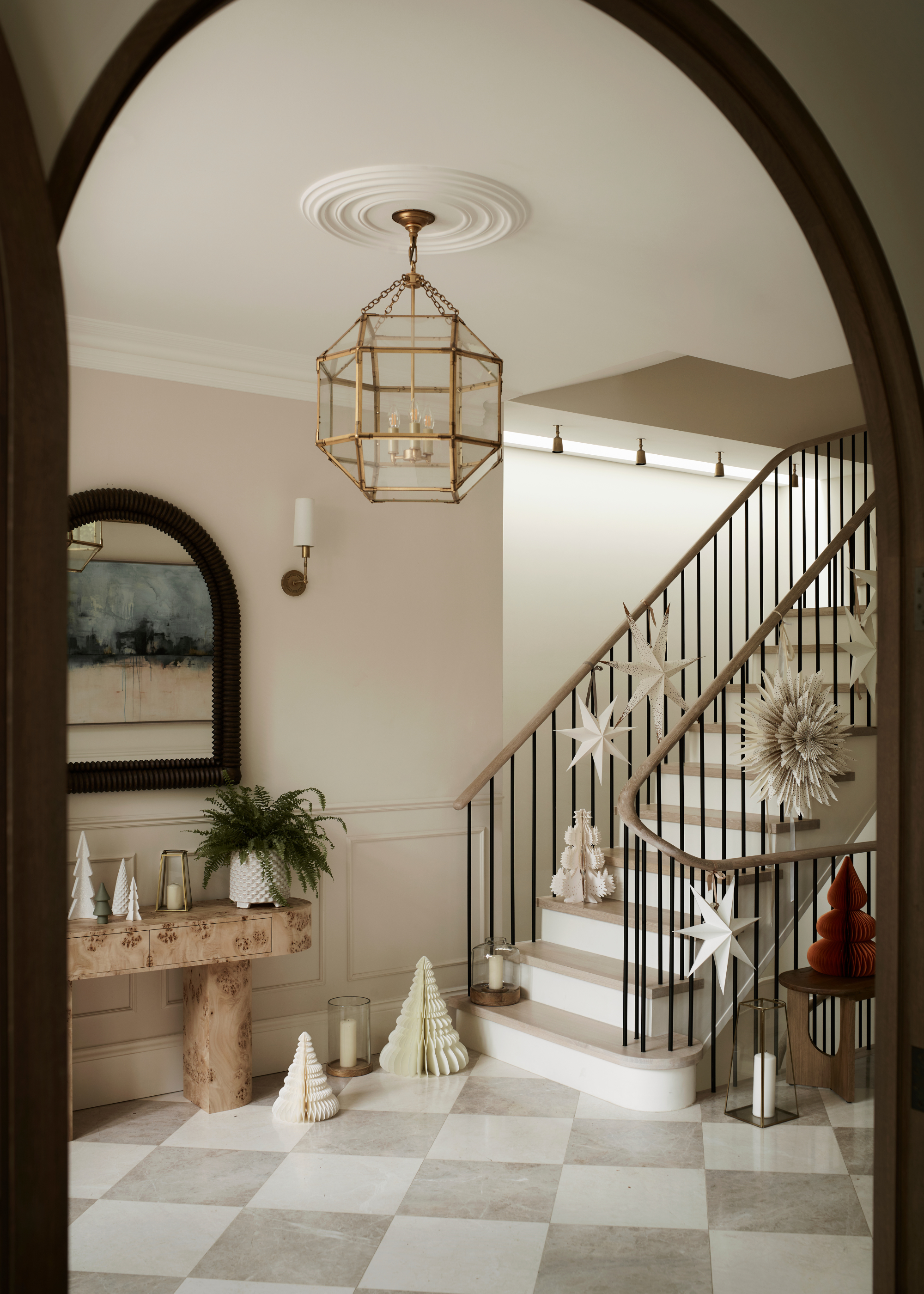 A neutral, modern christmas entryway with paper christmas decorations on the floor with glass lanterns and paper lampshades attached to the stair rails