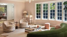 bright south-facing living room with plaster pink walls, green sofa, patterned armchairs, colorful stone coffee table, quirky console with lamp and decor, white-framed windows with lots of light pouring through