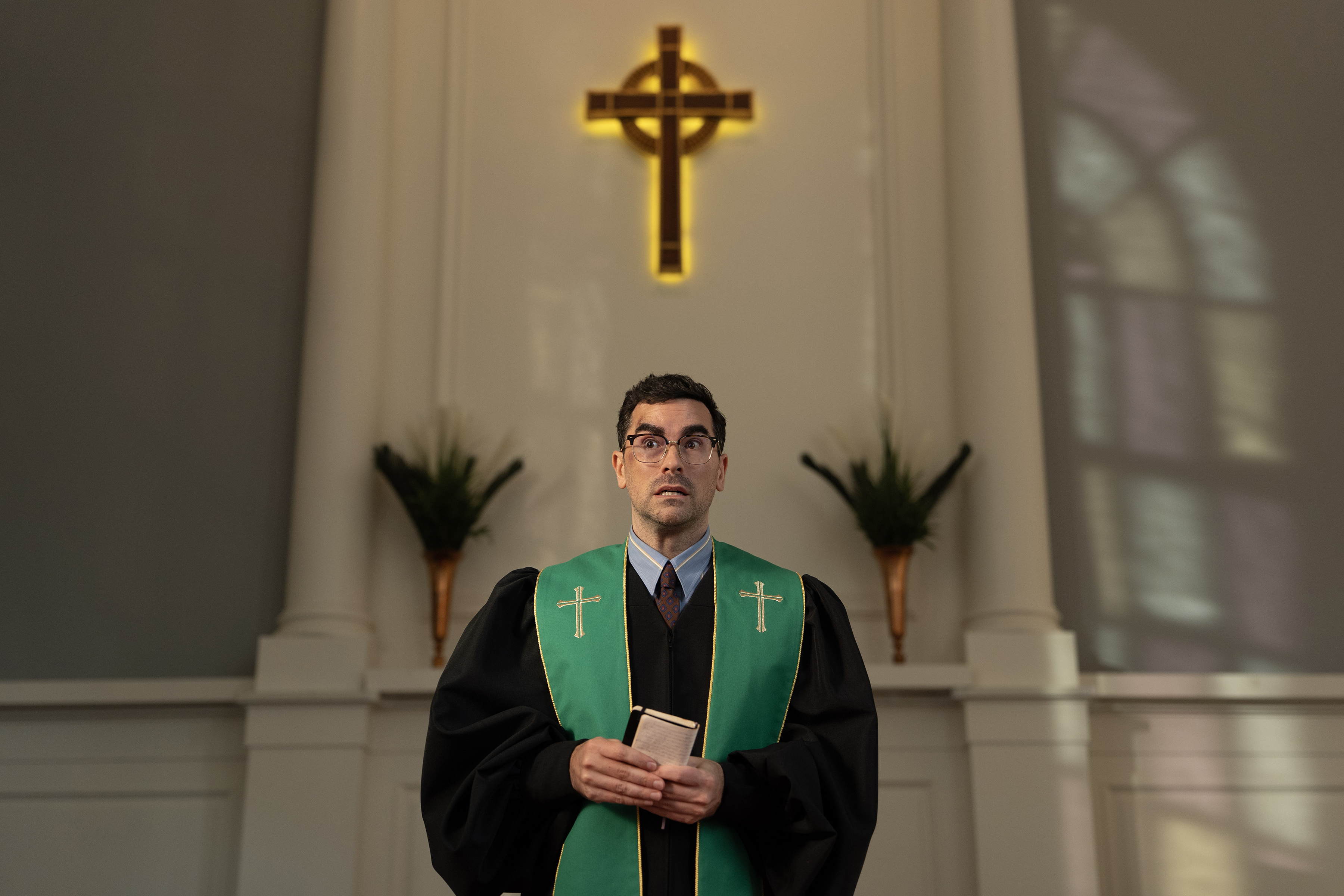 A pastor (Dan Levy as Nicky) stands in a church under a cross, in Episode 103 of BIG MISTAKES.
