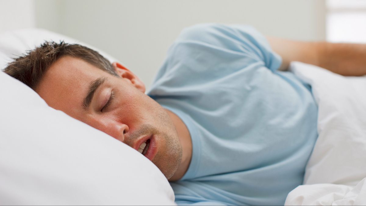 Man sleeping on his side with his mouth open snoring, which is a common symptom of obstructive sleep apnea