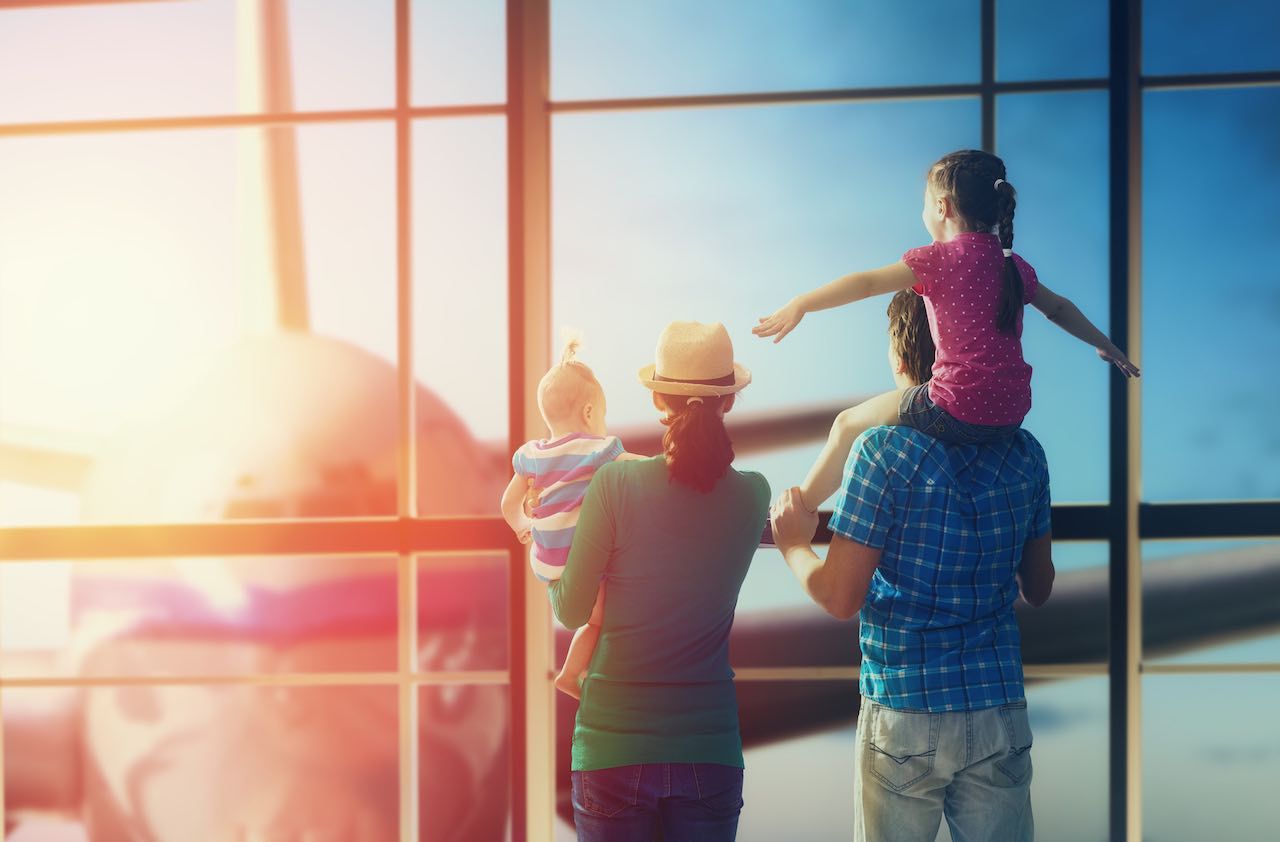 Happy family with children at the airport. Parents and their children look out the window at the plane.