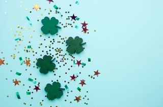 Happy St Patrick's Day in Irish—St. Patrick's Day flat lay, with golden confetti, green clover and drinks.