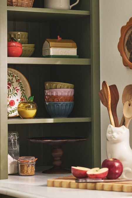 Charming vintage-inspired kitchenware from Molly Yeh's new Anthropologie collaboration styled atop a set of exposed olive green kitchen shelves