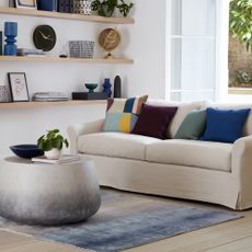 A living room with a cream sofa with contrasting cushions and a round ombre-effect coffee table with a matching rug